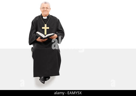 Christian priest reading the bible seated on panel isolated on white background Stock Photo