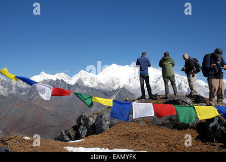 The Himalayan mountain of Kangchenjunga is framed by Buddhist prayer flags as trekkers photograph the mountain from a high point Stock Photo
