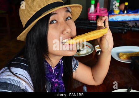 Thai woman eating Rice porridge or Congee with white deep-fried doughstick or sugar sponge cake Stock Photo