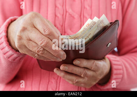 Elderly senior female old age pensioner taking ten pound notes GBP out of a money wallet to buy and pay for something with cash. England, UK, Britain Stock Photo