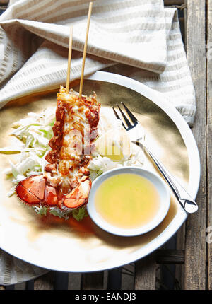 Main Lobster Tail skewered in the shell flash fried withe lemon butter and lemons and lettuce on a gold plate Stock Photo