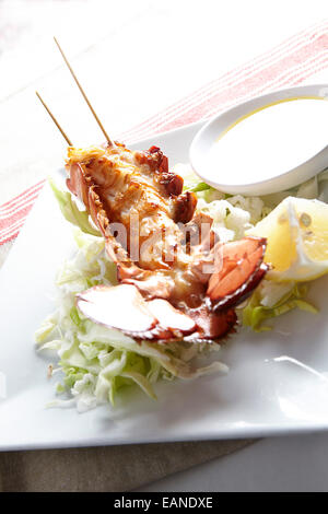 Main Lobster Tail skewered in the shell flash fried withe lemon butter and lemons and lettuce Stock Photo