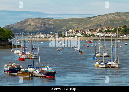 Boats moored on calm blue water of estuary of Conwy River with buildings of Welsh town of Conwy at base of adjacent hill Stock Photo