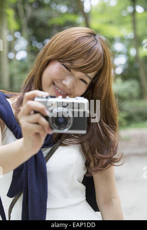 A woman in a Kyoto park holding a camera, preparing to take pictures. Stock Photo