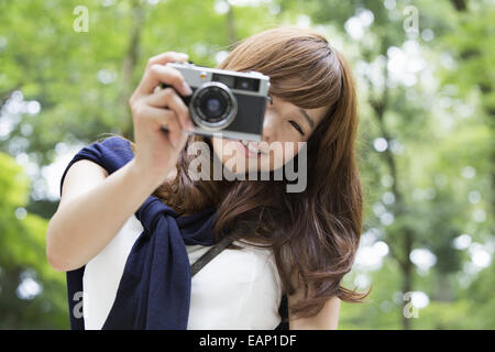 A woman in a Kyoto park holding a camera and laughing. Stock Photo