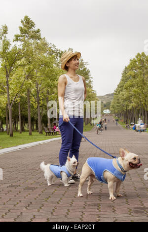 Woman walking two dogs on a paved path.