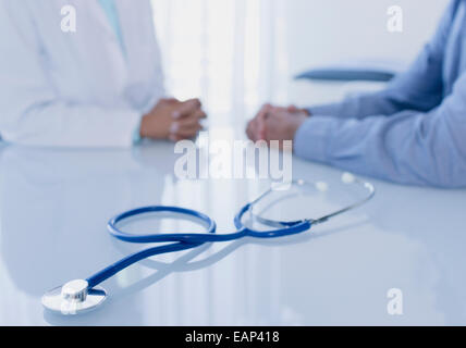 Stethoscope on white desk in doctor's office, female doctor and patient sitting in background Stock Photo