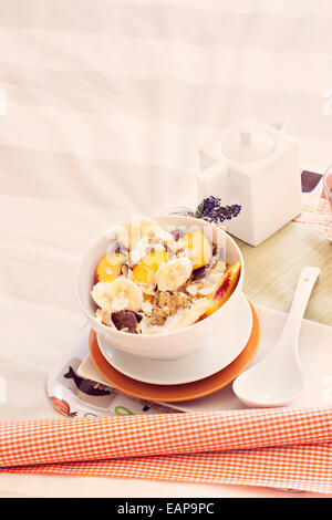 Breakfast in bed tray cereal, peach and banana, yogurt and tea, warm orange color. Stock Photo