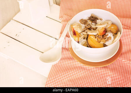 Breakfast in bed tray cereal, peach and banana, yogurt and tea, warm orange color. On white tablecloth and wood Stock Photo