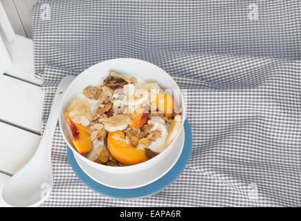 Breakfast in bed tray cereal, peach and banana, yogurt and tea, warm blue color. On white tablecloth and wood Stock Photo
