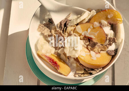 Breakfast in the sun, cereal bowl, peach and banana, yogurt on blue plate and warm vintage  color. White on wood Stock Photo