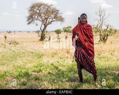 Maasai warrior dressed in traditional red clothes with rungu weapon in his hand, Mikumi National Park, Tanzania, East Africa. Stock Photo