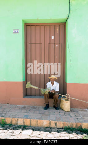 TRINIDAD, CUBA - MAY 8, 2014: An old broom street vendor seated at the door of a house Stock Photo