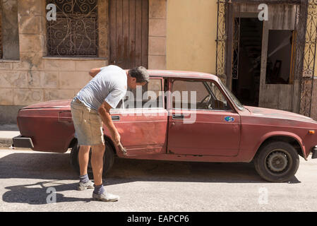 MATANZAS, CUBA - MAY 10, 2014:  On the street a man repair a battered door hammering your old car Stock Photo