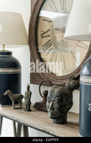 Detail of Chinese antiquities and tea canister lamps on wooden ledge with Old Clock on wall behind Stock Photo