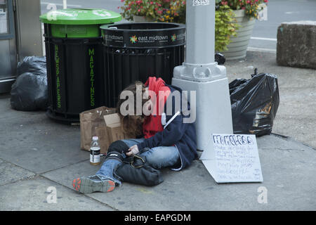Homeless person sleeping & reaching out with a sign for help on 34th and Broadway, NYC. Stock Photo