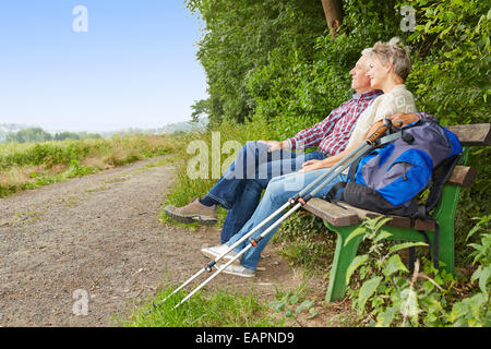 Senior couple taking a break on a bench while hiking in summer Stock Photo