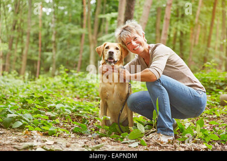 Labrador Retriever sitting with elderly woman in a forest Stock Photo