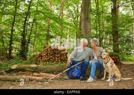 Two seniors on a hike with dog in a forest taking a break Stock Photo
