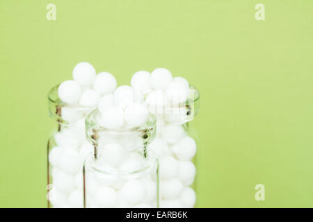 Closeup image of homeopathic medicinal pills (made from an inert substance - sugar/lactose) in bottles on a green background. Stock Photo