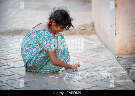 Girl creating a traditional Rangoli, Kolam or Muggu, decorative pattern made of coloured sand, outside a door, Rameswaram Stock Photo