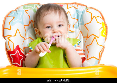 happy baby child sitting in chair with a spoon Stock Photo