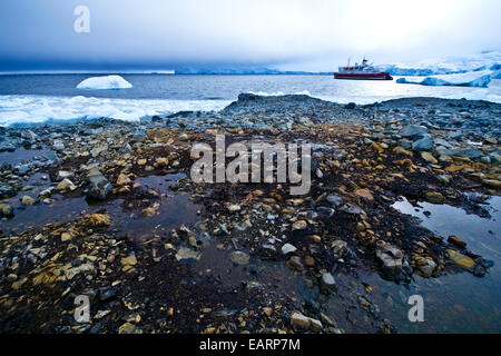 An Antarctic cruise ship anchored in an icy bay off a rocky shore. Stock Photo