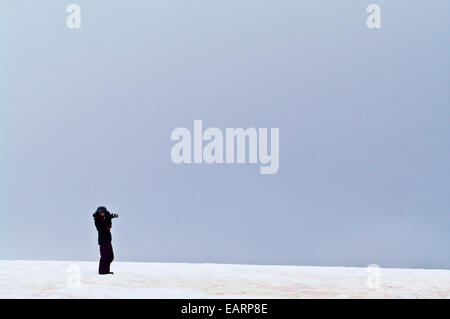 A lone tourist photographing on a windswept hillside in Antarctica. Stock Photo