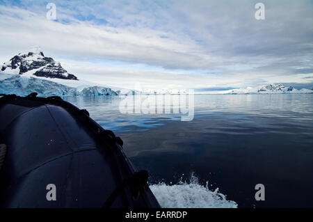 The bow of a boat glides over calm icy seas between snow-capped peaks. Stock Photo