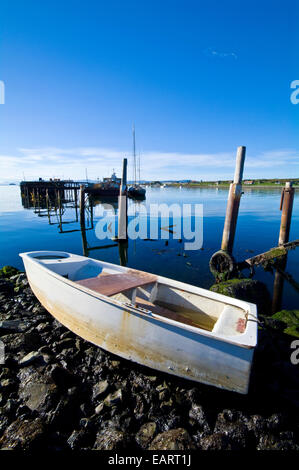 A small paddle boat beached on the rocky shore of a fishing village. Stock Photo