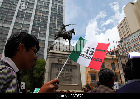 La Paz, Bolivia. 20th November, 2014. A protester holding a Mexican flag with 43 Ayotzinapa on it passes a statue of Simón Bolivar during a march to demand justice for the 43 missing students in Mexico and protest against the Mexican government's handling of the case and corruption. Today has been designated a Global Day of Action for Ayotzinapa; a national strike is planned in Mexico and many protests are taking place worldwide to show support. The students disappeared after clashing with police on the night of 26th September in the town of Iguala. Credit:  James Brunker / Alamy Live News Stock Photo