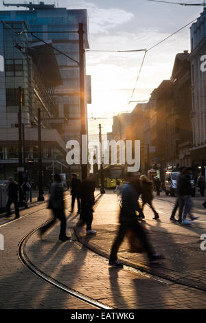 Manchester cityscape, Low evening winter sun in Fountain street, near Piccadilly Gardens, Shoppers silhouetted against the sun producing long shadows crossing the road as they enjoy a fine sunny end to the day in Manchester. Manchester Metrolink city centre tram lines & route. Stock Photo