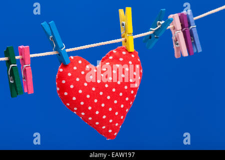 red heart hanging on a clothesline with clothespins, blue background Stock Photo