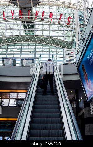 A man rides an escalator to an upper level in a shopping mall. Stock Photo