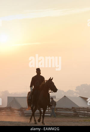 A man dressed in Civil War era attire rides his horse at sunrise. Stock Photo