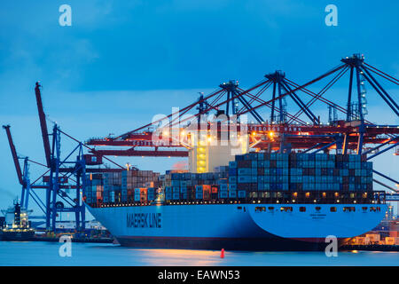 Large ship carrying cargo in a harbour at dusk Stock Photo
