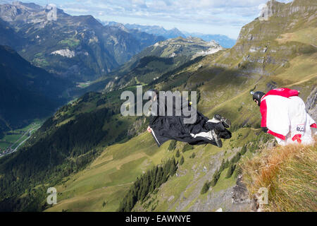 BASE jumper is exiting from a cliff down into the deep valley. Thereby he is within a wingsuit to fly fare away from the rock. Stock Photo