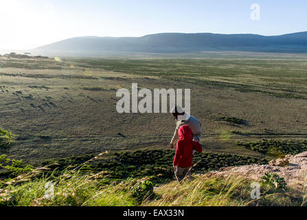 A safari guide assists a small child to climb down the steep surface of a rocky outcrop. Stock Photo