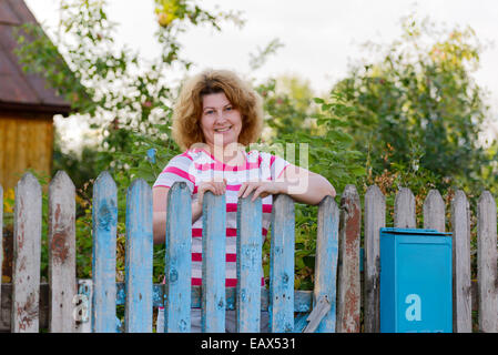 middle-aged woman stands at the gates country house Stock Photo