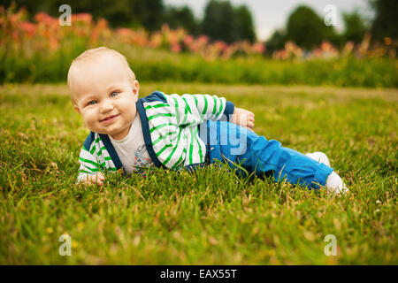 Cute baby looking at camera and smiling while lying on the grass outdoors in sunlight Stock Photo