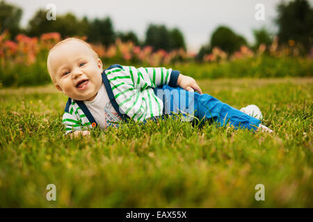 Cute baby looking at camera and smiling while lying on the grass outdoors in sunlight Stock Photo