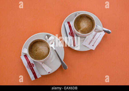 Coffee cups with teaspoon saucer and biscuits on an orange coloured table sugar packets Stock Photo