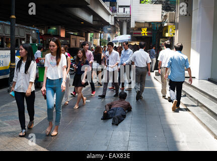 Handicapped Beggar on Silom road, Bangkok, Thailand as middle class people walk by. Stock Photo