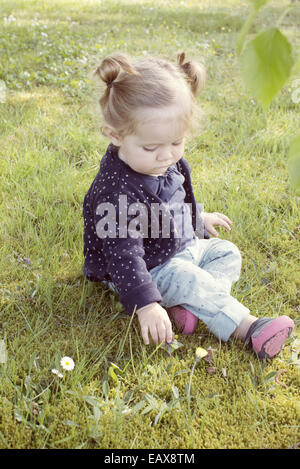 Baby girl sitting on grass, picking flower Stock Photo