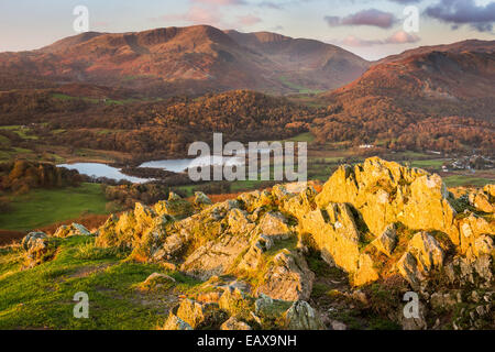 First light strikes rocks on the summit of Loughrigg Fell, looking across Elter Water towards Wetherlam. Lake District NP Stock Photo