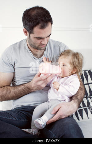 Father holding baby girl on lap, feeding her with bottle