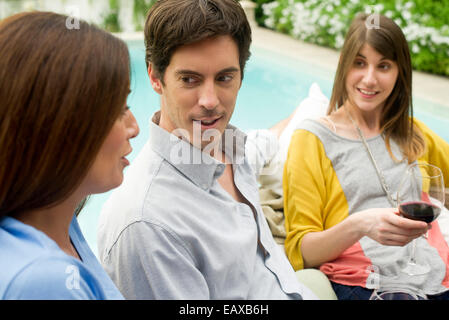 Friends relaxing together by pool with glass of wine Stock Photo