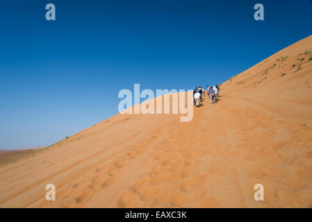 Hikers climbing up a sand dune in the Empty Quarter, Oman. Stock Photo