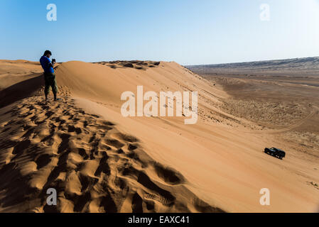 A young man video recording a four-wheel drive jeep driving over sand dunes in the desert of Oman. Stock Photo