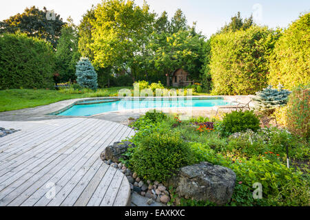 Backyard rock garden with outdoor inground residential swimming pool, curved wooden deck and stone patio Stock Photo